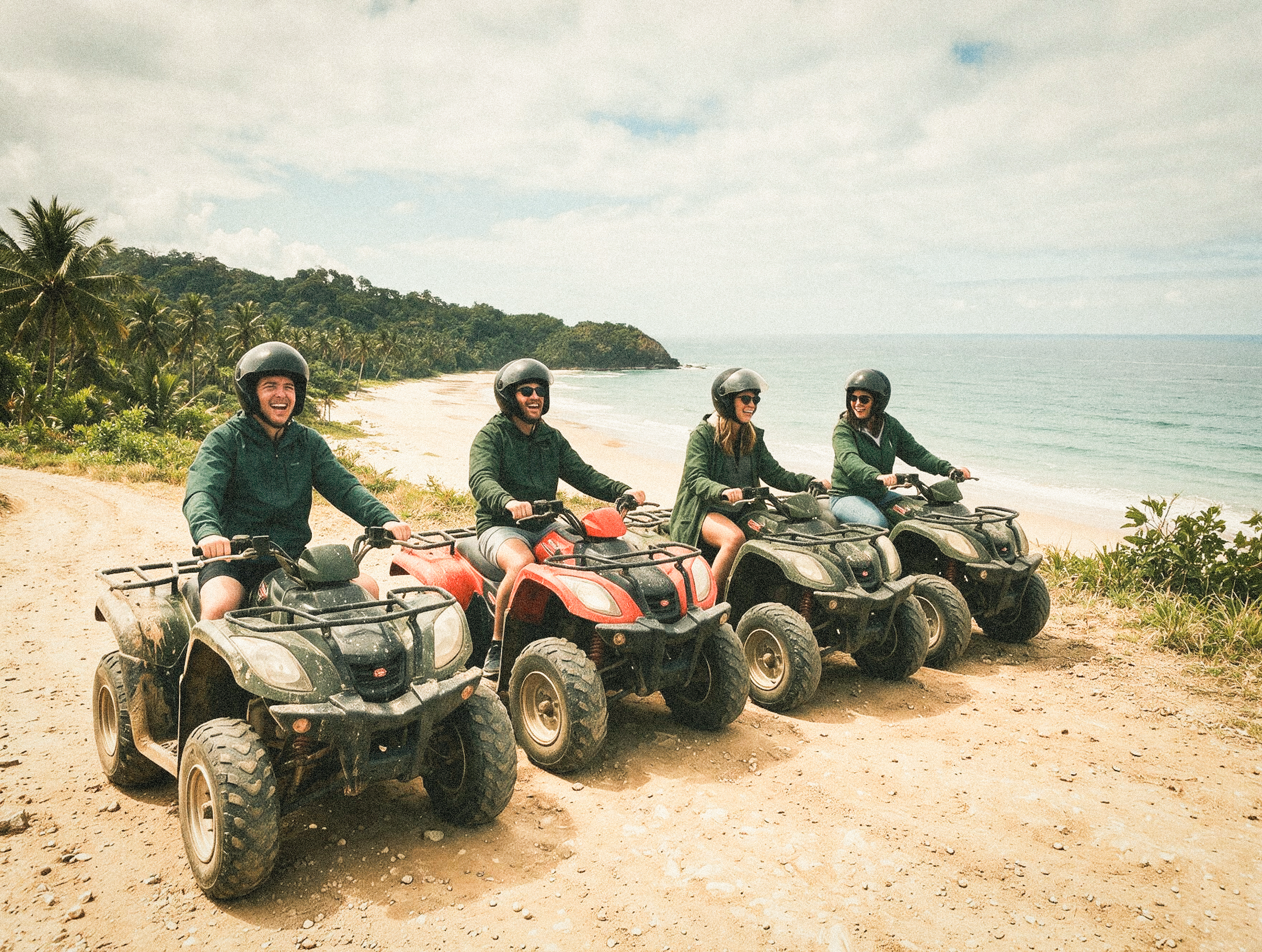 A small group rides all-terrain vehicles along a red dirt trail above the coastline.