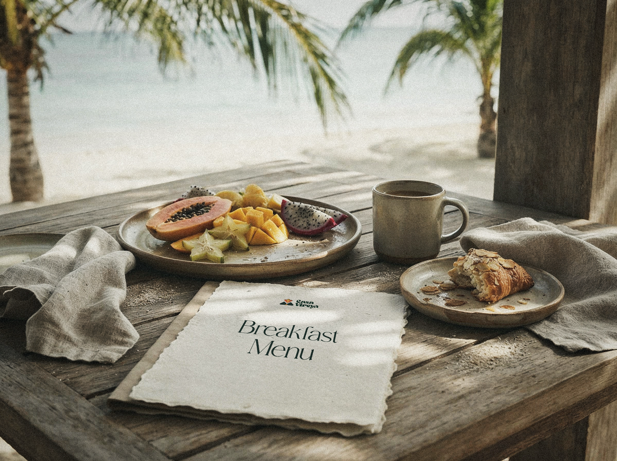 A handwritten breakfast menu beside a plate of tropical fruit and a warm pastry.