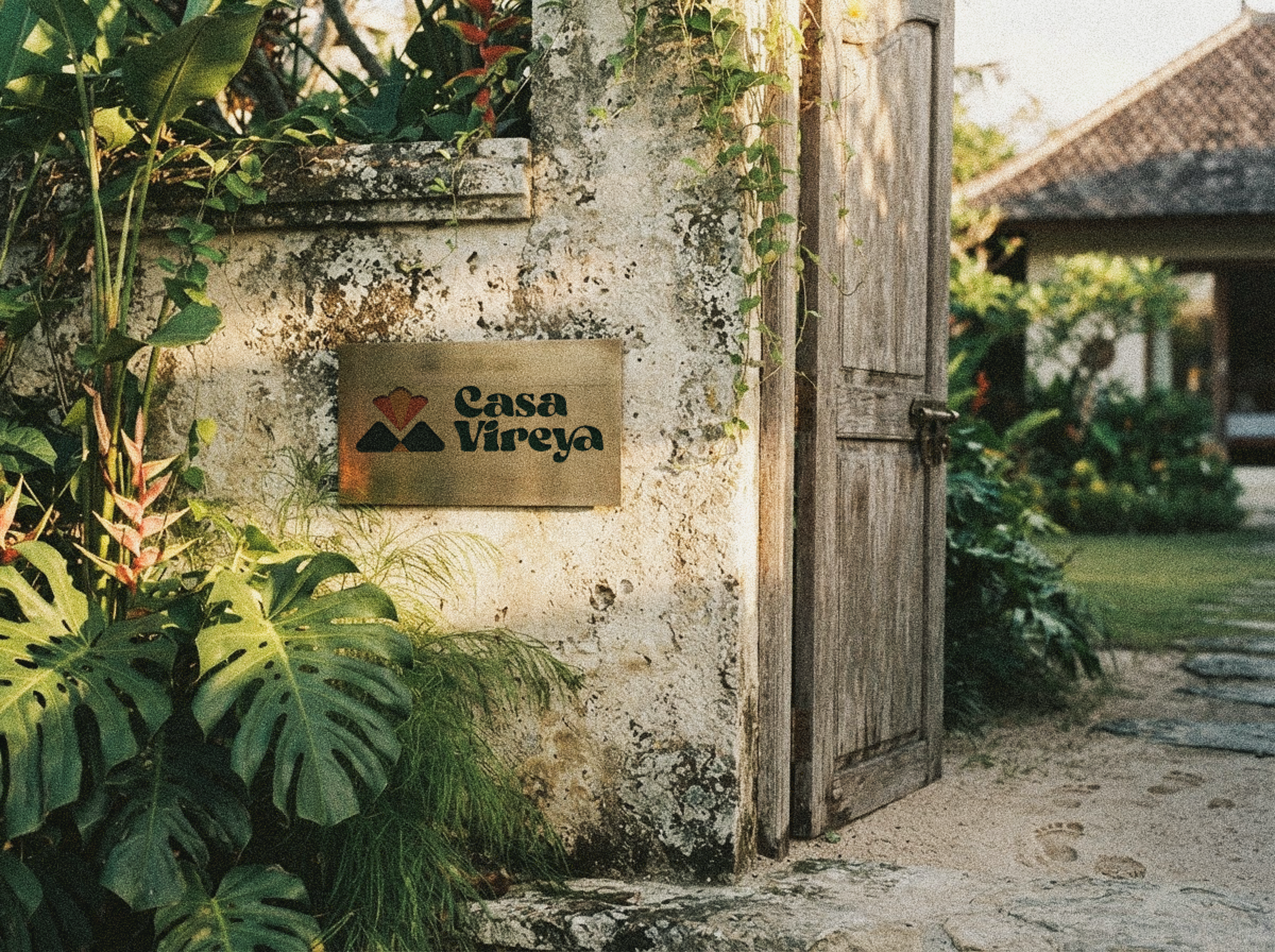 A brass Casa Vireya sign mounted on a weathered stone wall, half-hidden by tropical leaves.