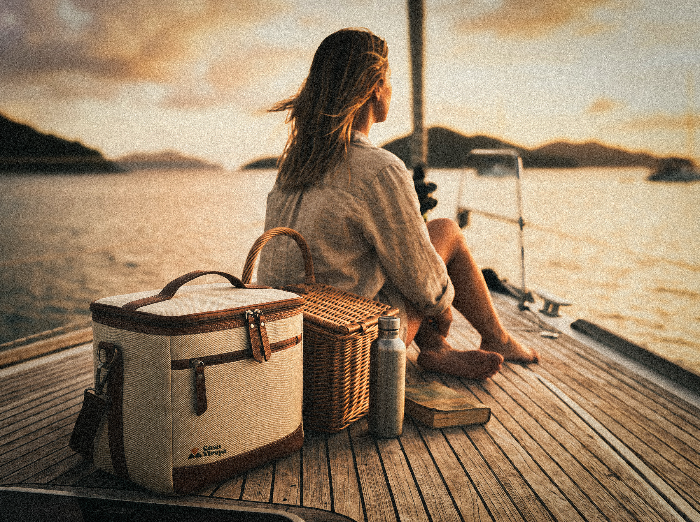 A woven picnic basket and cooler bag set on a wooden deck at golden hour.